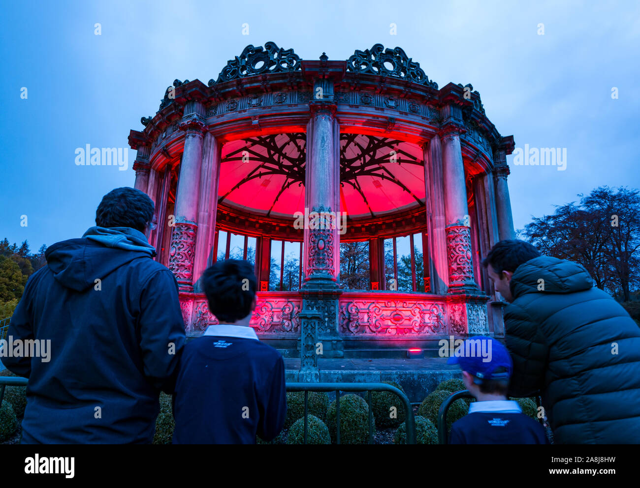 Dalkeith Country Park, Dalkeith, Midlothian, Scotland, Regno Unito, 9 novembre 2019. Papavero scozzese appello: Il Papavero Scozia illuminazione di campagna Red ha più di 120 edifici e strutture in tutta la Scozia illuminato in rosso nella settimana in esecuzione fino al Giorno del Ricordo. Gli ornati rovinato Orangerie è illuminato in rosso come l'oscurità cade. L'Orangery dispone di dodici lati con colonne doriche. Nella foto: Angus, Sam, Finn & Barry ammirare la struttura Foto Stock