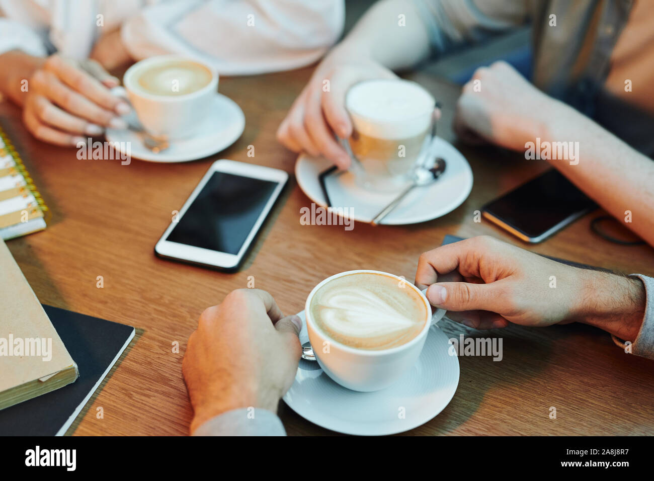 Le mani di amici radunati da tavolo in legno nel cafe e avente cappuccino Foto Stock