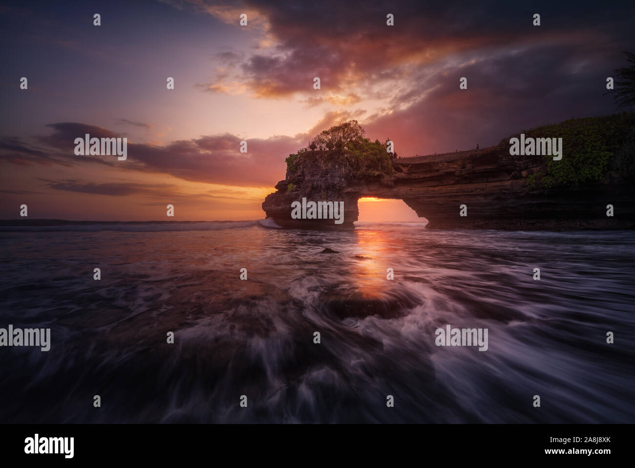 Pura Batu Bolong, un tempio indù su una scogliera arch, nel sud di Bali, Indonesia. Nuvoloso Tramonto e le onde sulla spiaggia nelle vicinanze. Foto Stock