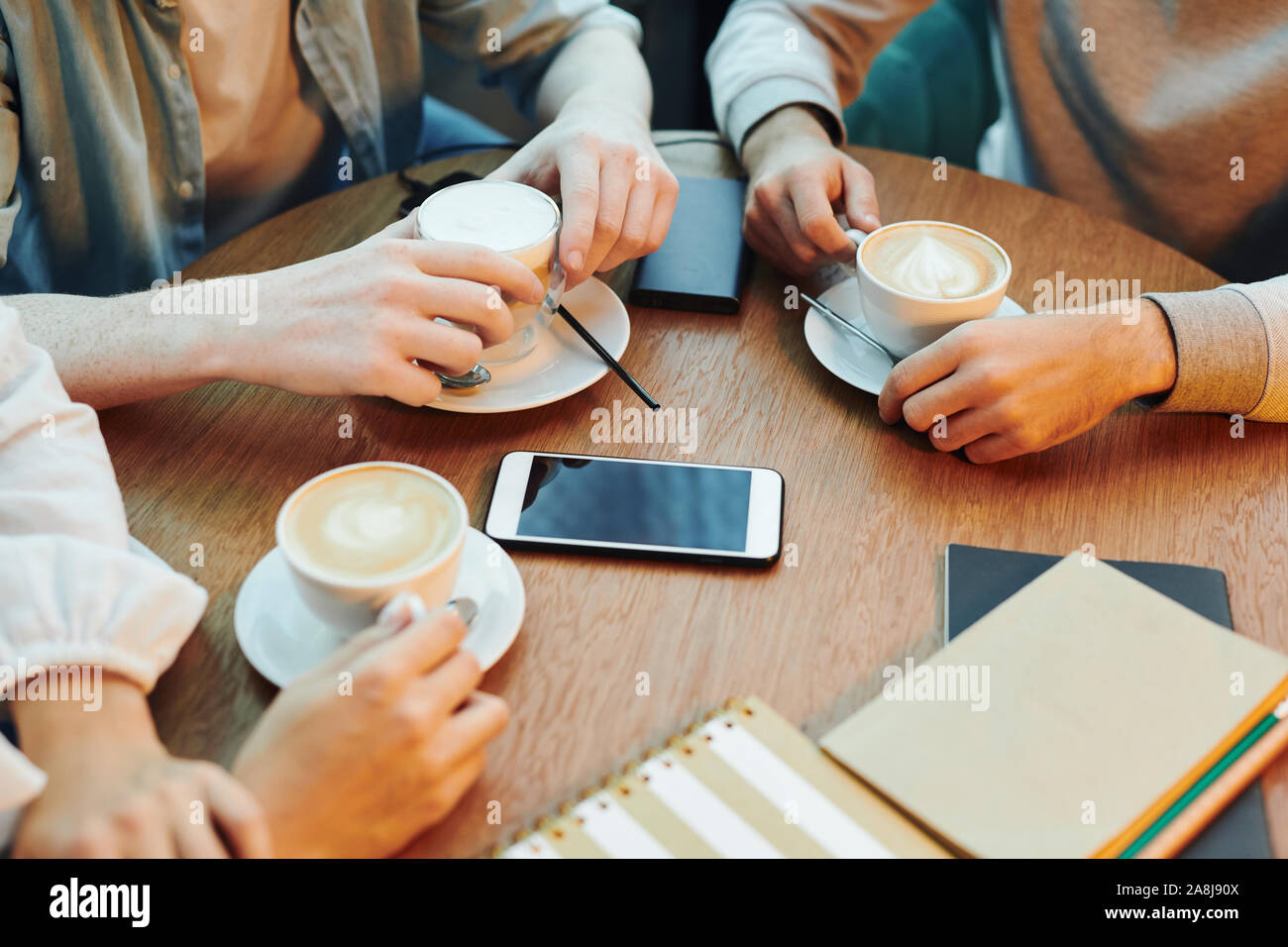 Le mani del collegio di amici seduti a un tavolo di legno in cafe e avente cappuccino Foto Stock