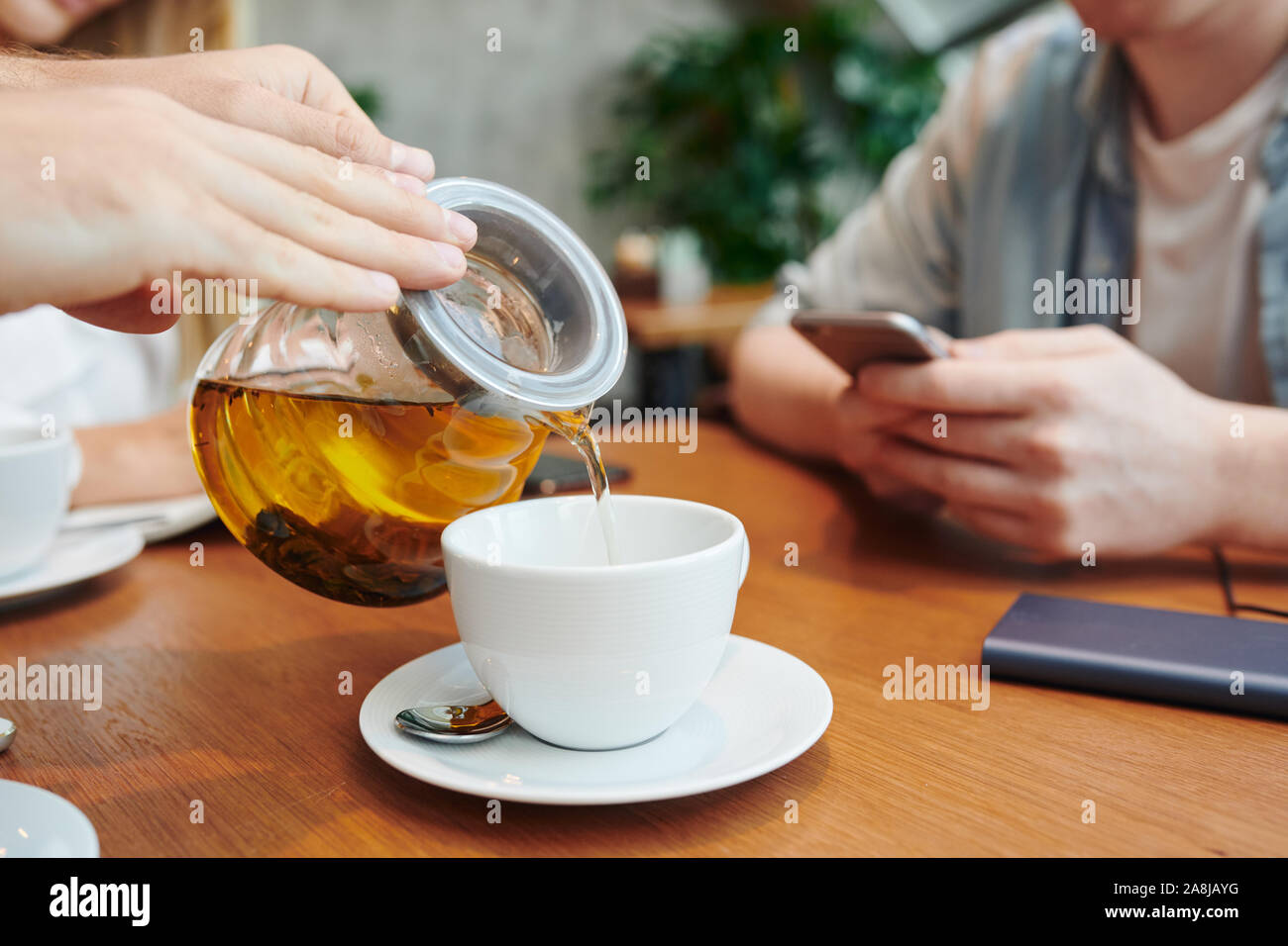 Le mani del ragazzo con teiera versando il tè alle erbe in porcellana bianca cup in cafe Foto Stock