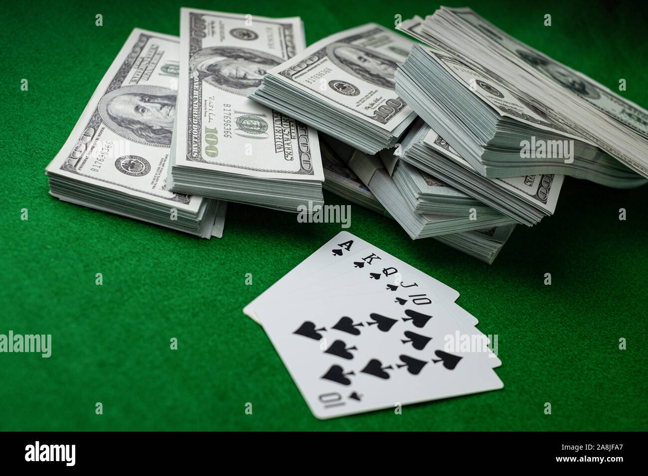 Poker Casino Gambling Royal Straight Flush e la pila di denaro di 100 dollari USA banconote presso lo sfondo verde, giocando card club 5 carte Foto Stock