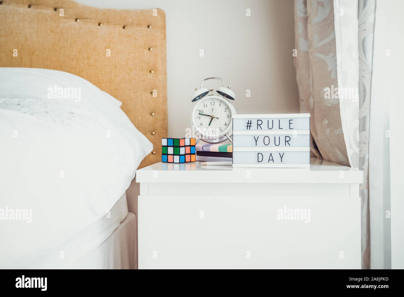 Ispirazione vita motivazionali citazioni hashtag regola il tuo giorno messaggio sulla casella alleggerita con sveglia, notebook e Magia cubo sul comodino Foto Stock