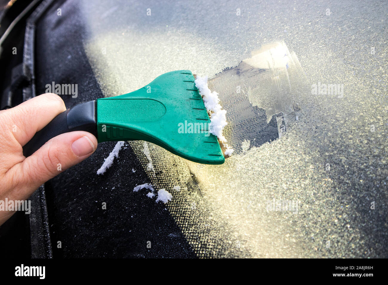 Vista ravvicinata della persona che raschia il ghiaccio dal parabrezza dell'auto con il raschiatore all'inizio dell'autunno mattina nel Nord Europa. Foto Stock
