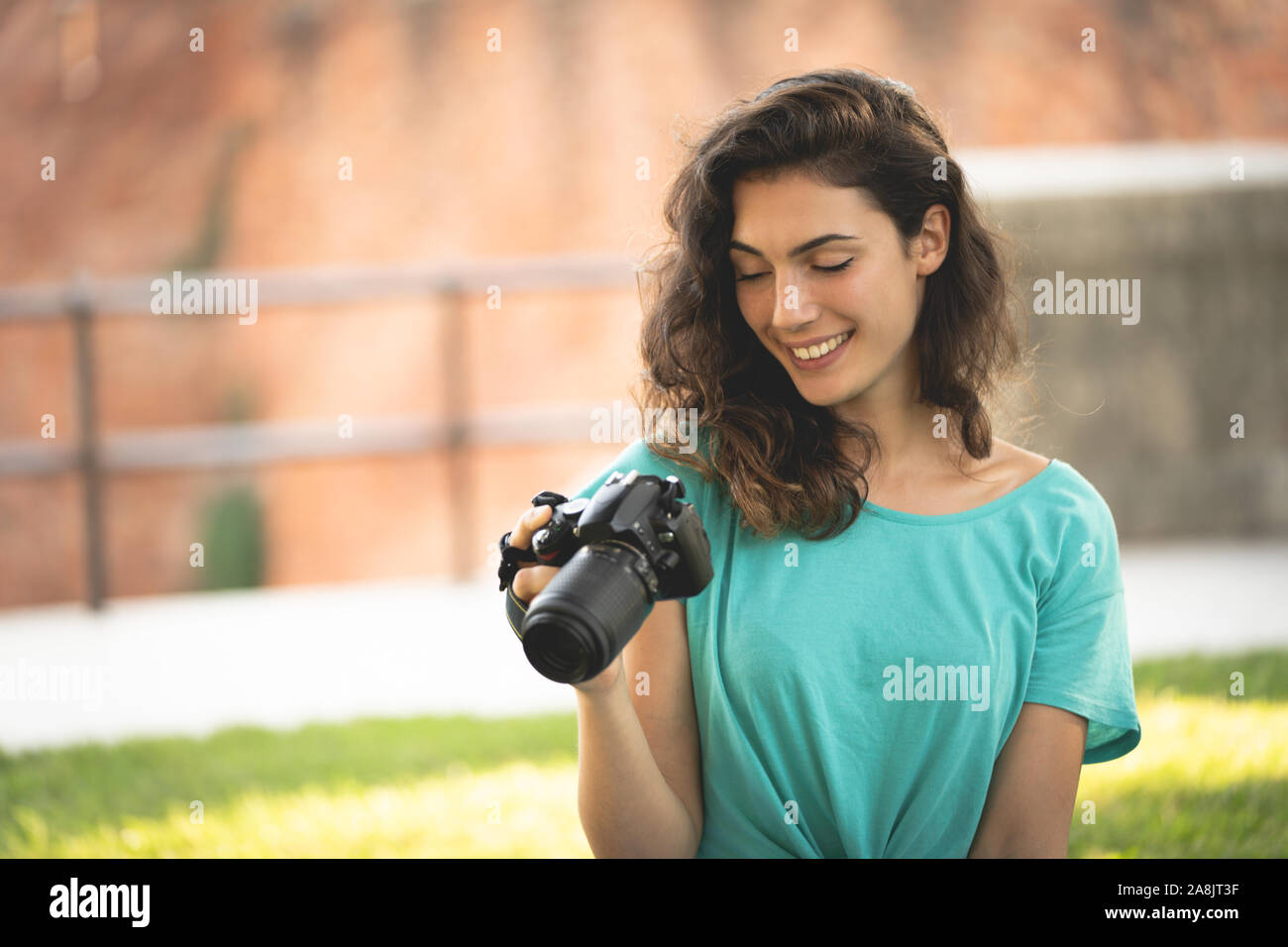 Fotografo ragazza seduta sul prato guardando lo schermo della fotocamera, sorridente Foto Stock