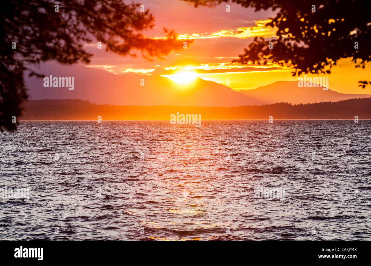 Il sole che tramonta oltre le montagne olimpiche e Puget Sound come visto da ovest vicino Seattle Alki Beach, Washington, Stati Uniti d'America. Foto Stock