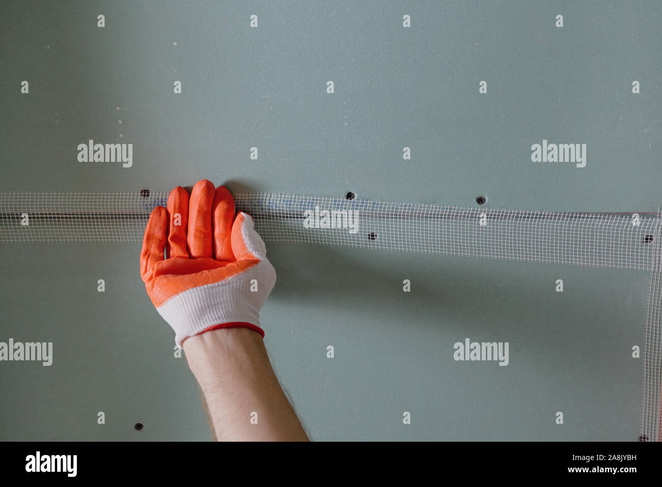 Un lavoratore è di attaccare la maglia per le giunzioni tra i plasterboards. Foto Stock