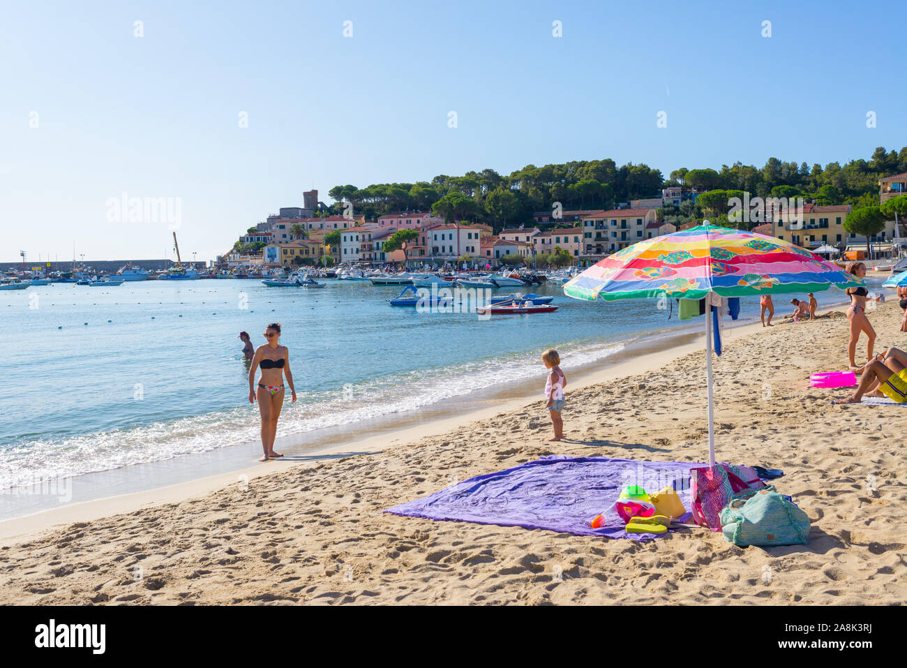 Marina di Campo, Isola d'Elba, Italia - Settembre 2019: la gente sulla spiaggia di Marina di Campo con il porto e il villaggio in background Foto Stock