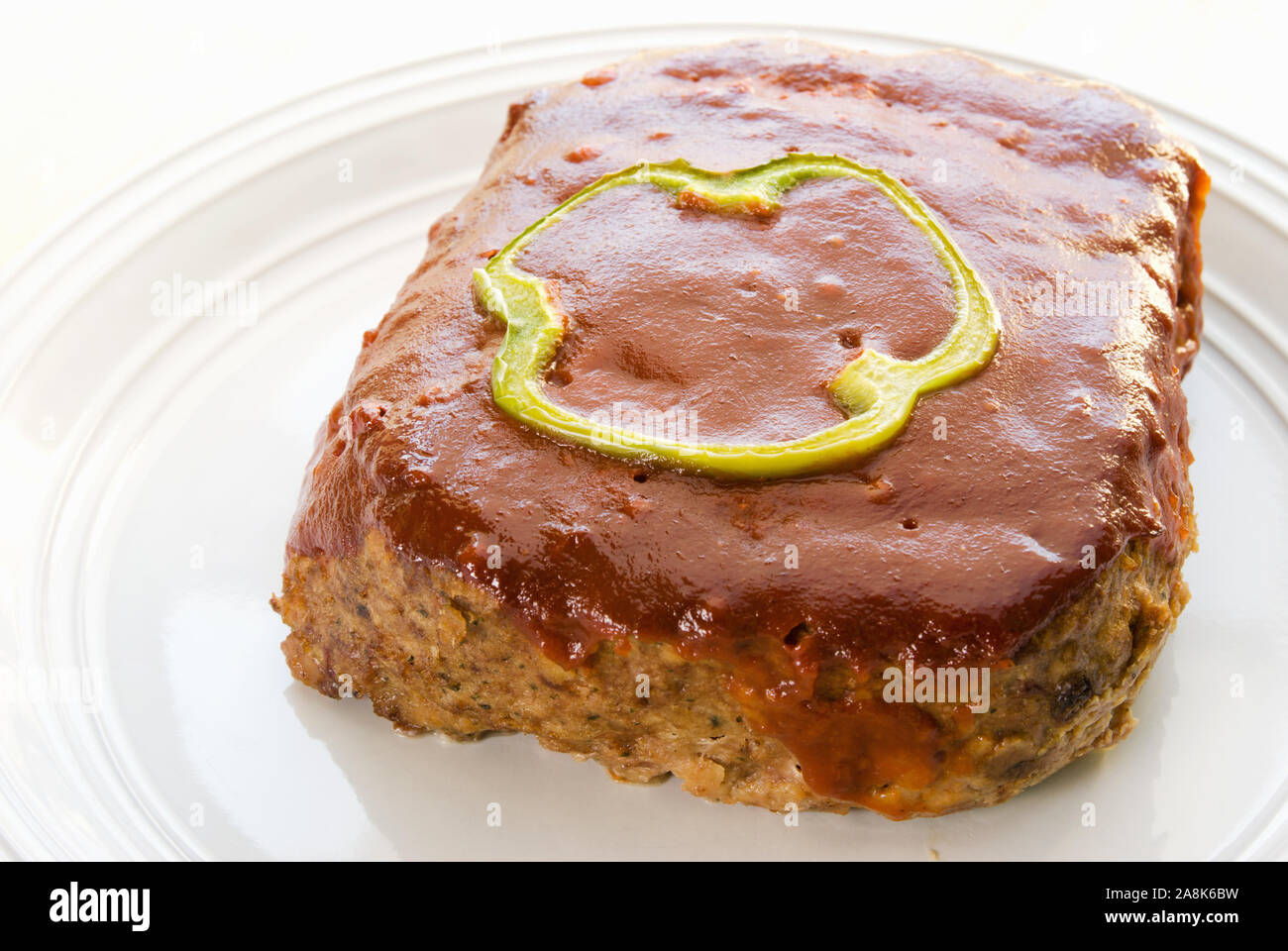 Freschi Fatti in casa a base di carne cotti al forno pane condito con una fetta di peperone verde e una base di ketchup salsa. Questo delizioso pasto viene servito su una piastra bianca. Foto Stock