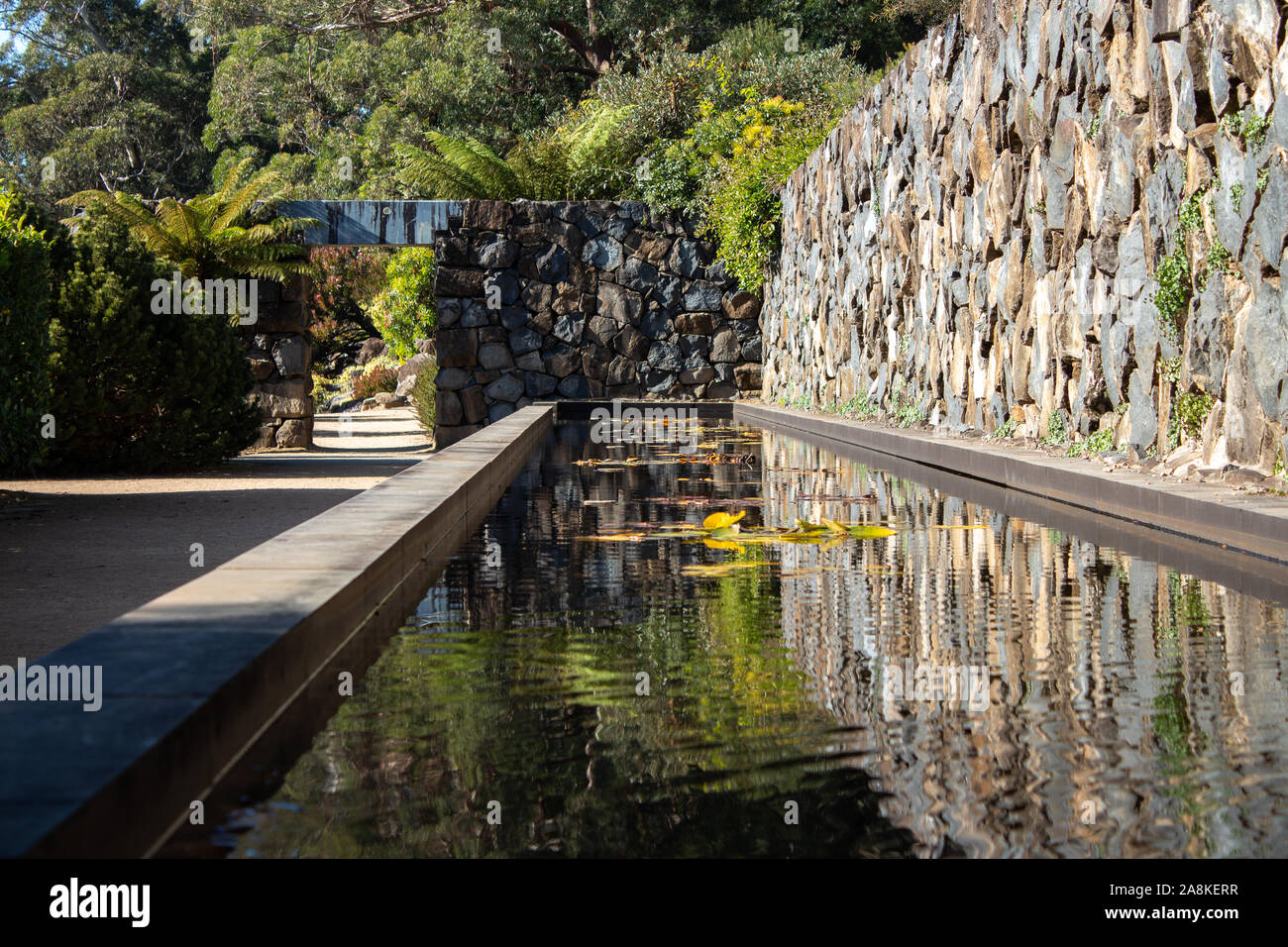 Giardino acqua caratteristica dello stagno con funzione di roccia parete, ninfee, arco porta lungo la passerella di pietra circondato da alberi Foto Stock