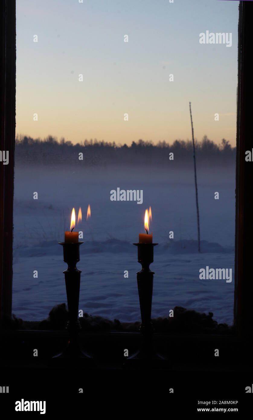 Due candele in una finestra. Fuori è un paesaggio invernale, cielo blu e del crepuscolo. La lana di pecora è utilizzato come decorazione tra esterno e interno di windows. Foto Stock