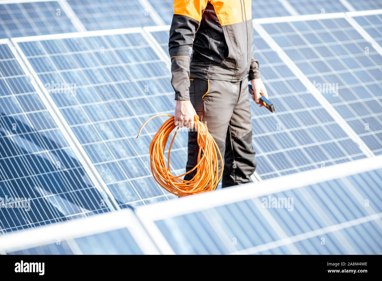 Ben attrezzato lavoratore in arancione di protezione abbigliamento manutenzione pannelli solari su un tetto fotovoltaico impianto. Concetto di manutenzione e installazione di stazioni solari Foto Stock