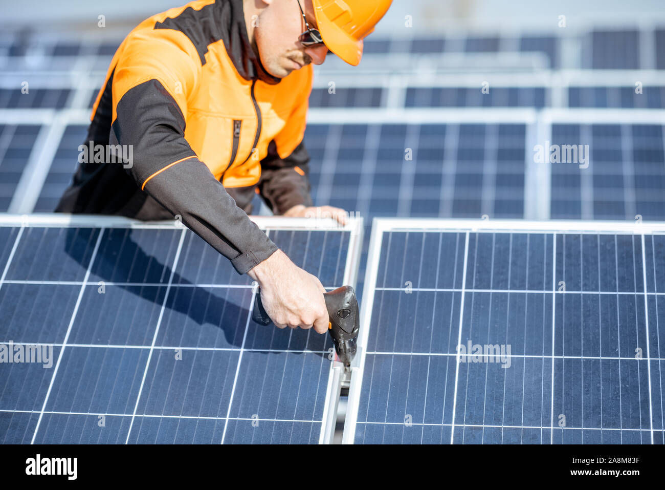 Ben attrezzato lavoratore in arancione di protezione abbigliamento installazione o sostituzione pannello solare su un tetto fotovoltaico impianto. Concetto di manutenzione e installazione di stazioni solari Foto Stock