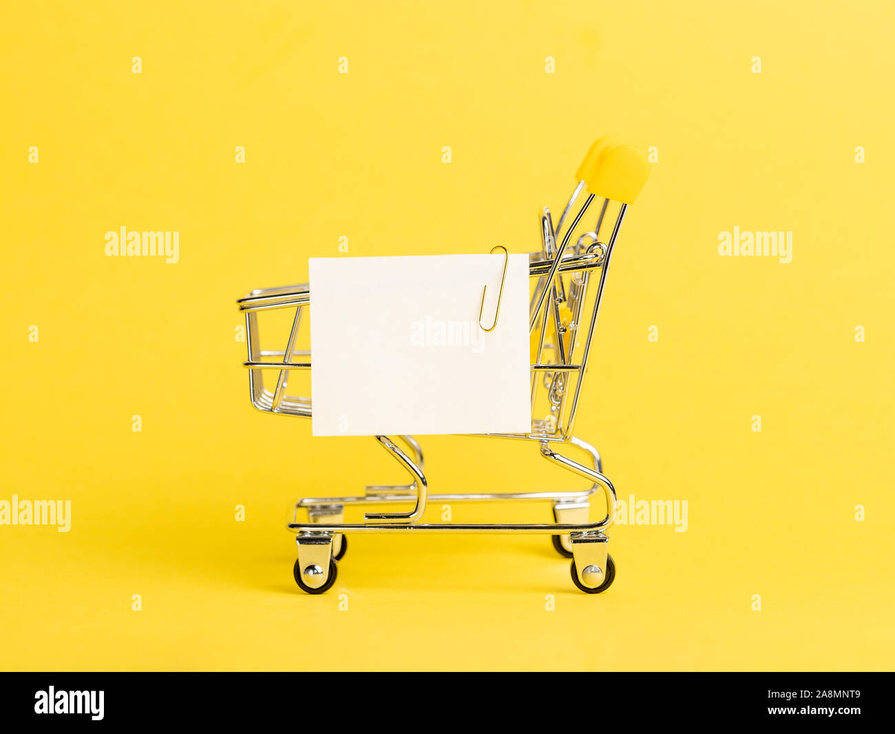 Carrello spesa e white paper nota elenco su sfondo giallo. Il concetto di shopping su giallo luminoso dello sfondo. Vuoto di carta bianca nota su carrello. Copia spazio per il testo o il design. Foto Stock