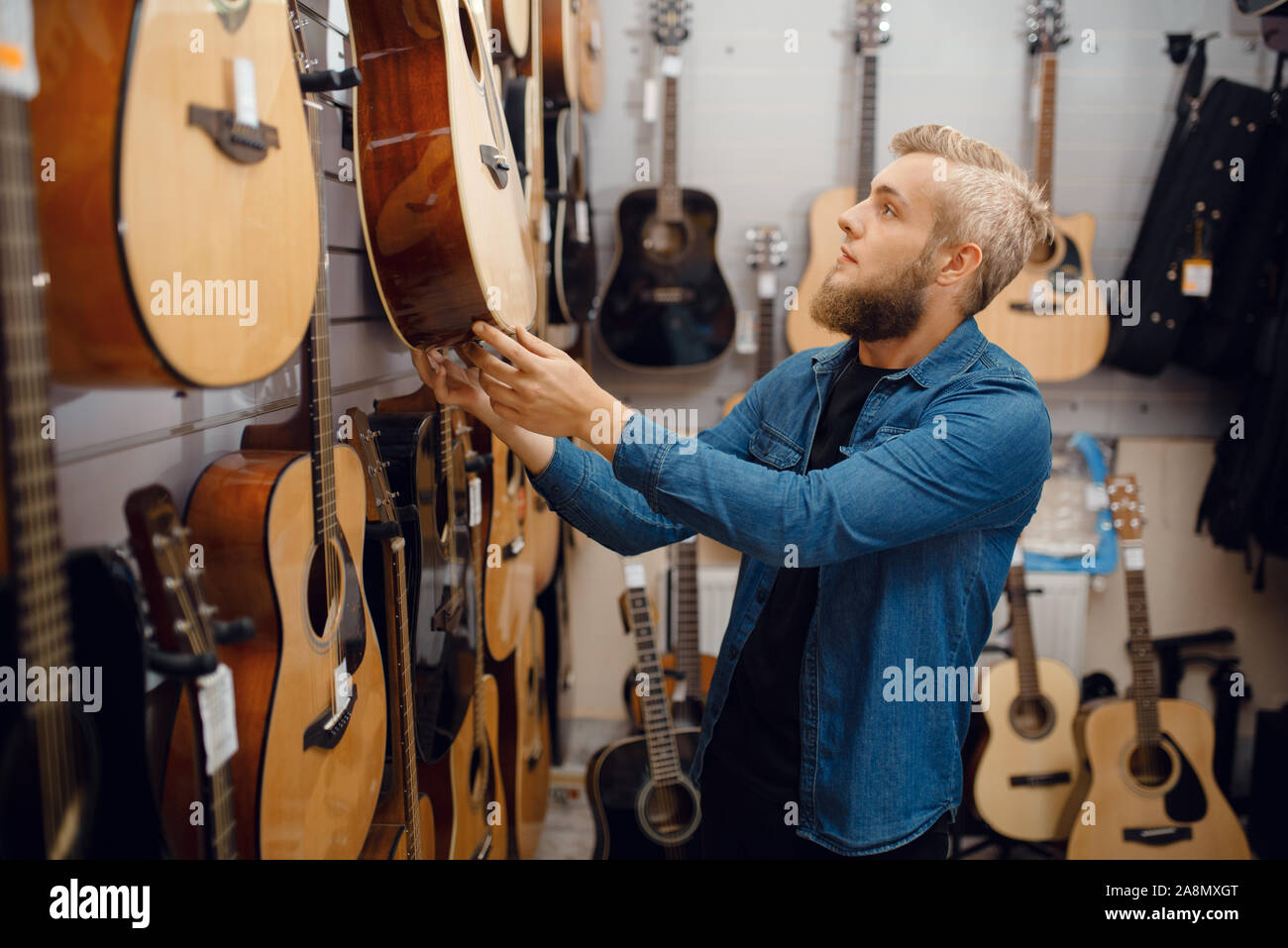 Barbuto giovane scegliendo una chitarra in music store Foto Stock