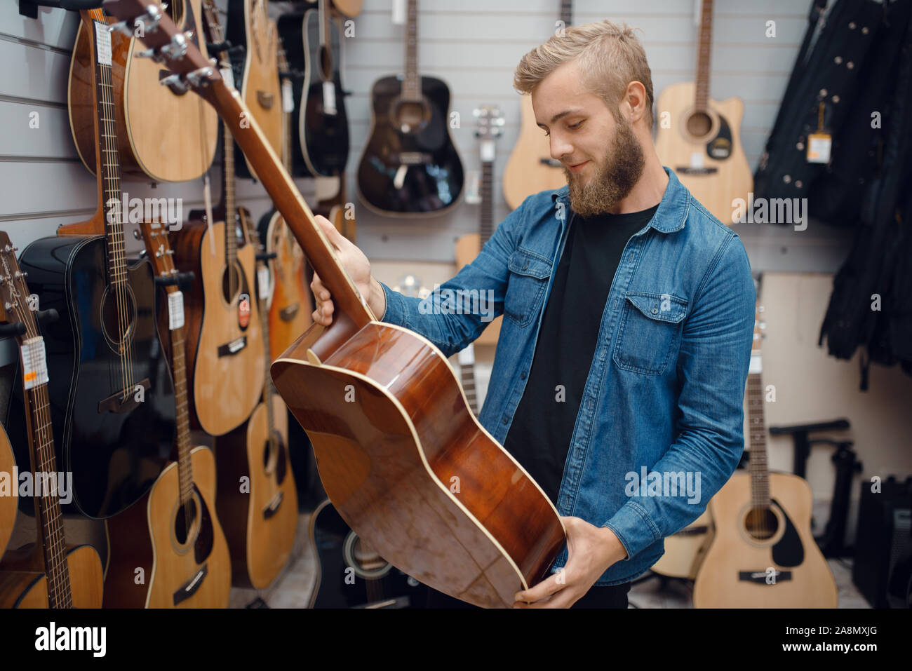 Barbuto giovane scegliendo una chitarra in music store Foto Stock