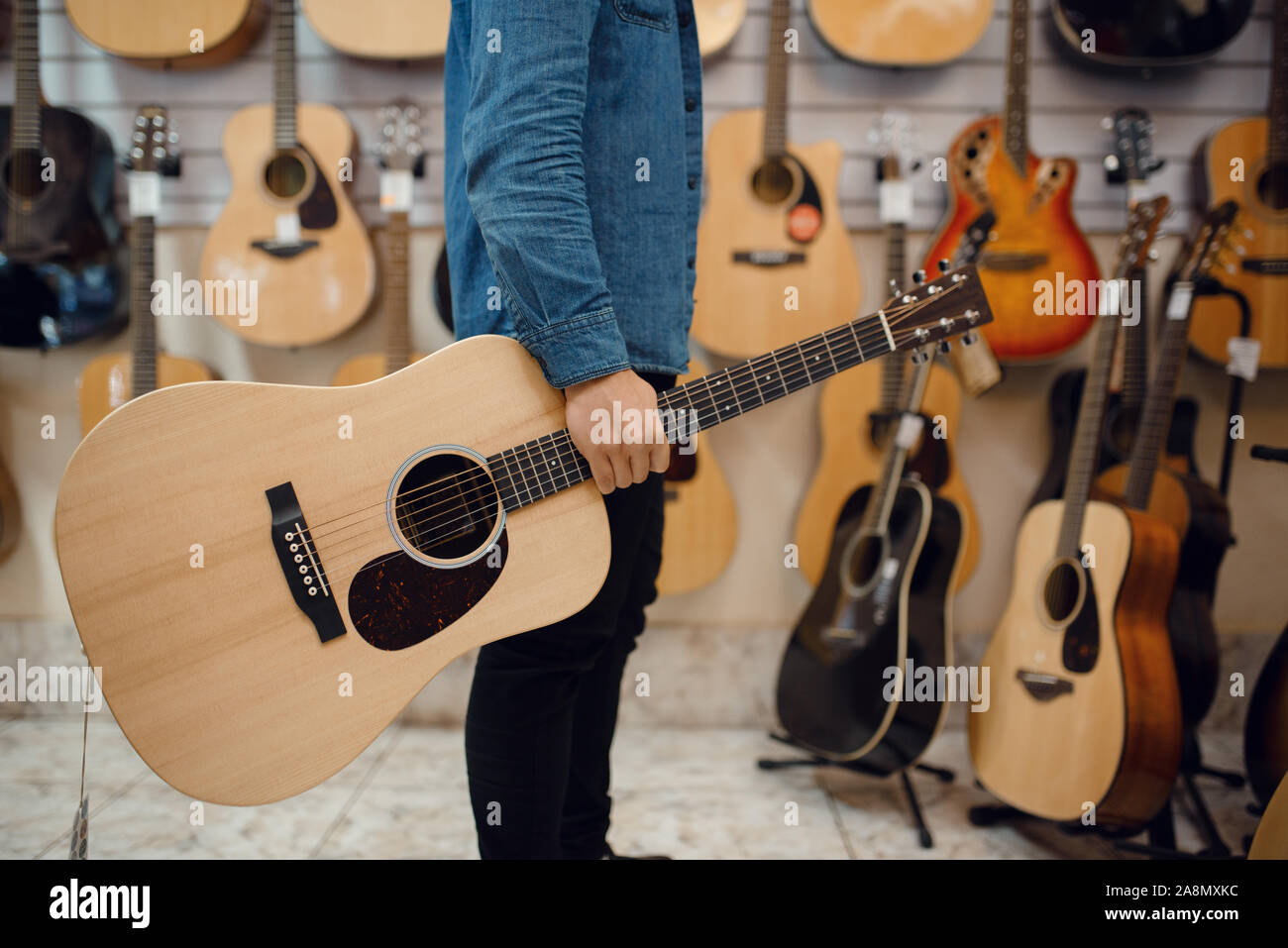 Giovane uomo tenendo la chitarra acustica in music store Foto Stock