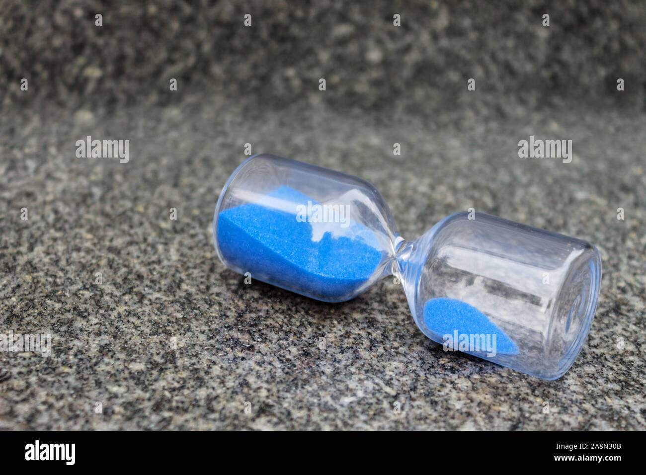 La clessidra di vetro con granuli blu giacciono su granito grigio Foto Stock