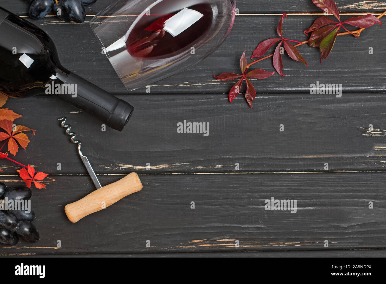 Bottiglia di vino rosso, bicchiere di vino, cavatappi e autunno foglie rosse sui tavoli in legno nero Foto Stock