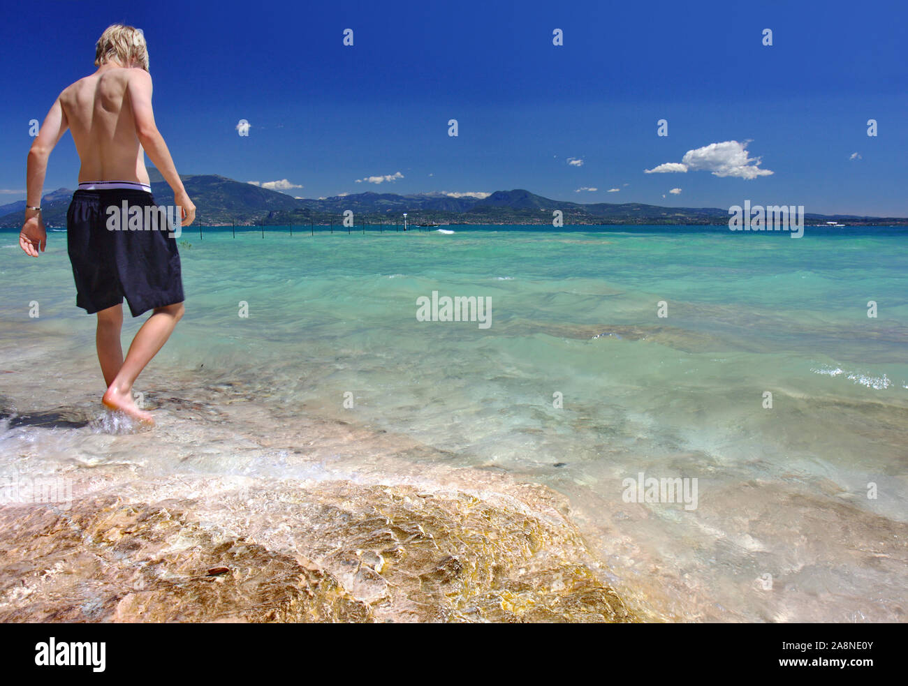 Un ragazzo nuota sulla spiaggia sulle rive del lago di Garda vicino a Sirmione town, Italia Foto Stock
