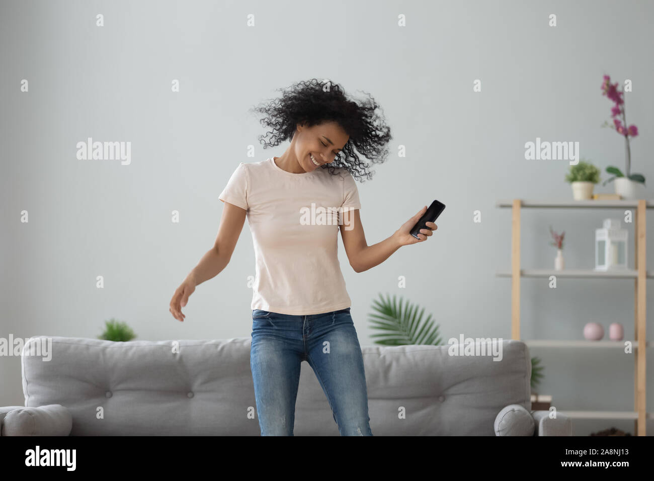 Emozionato americano africano donna saltare, ballare, usando il telefono Foto Stock