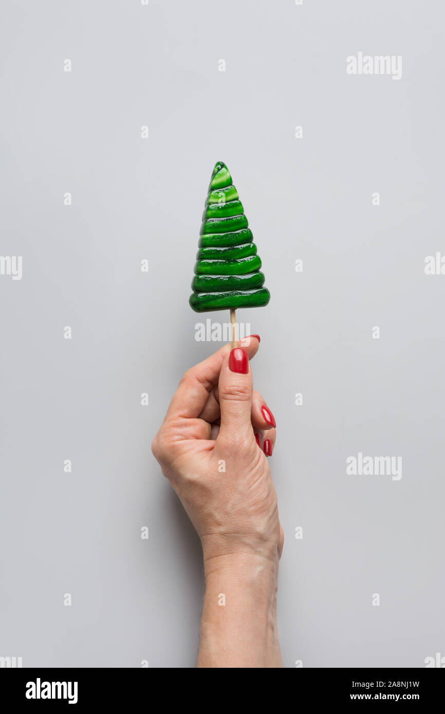 Femmina tenendo la mano di Natale a forma di albero lecca-lecca. Close up. Xmas greeting card. Splendida vacanza manicure con unghie rosse. Foto Stock