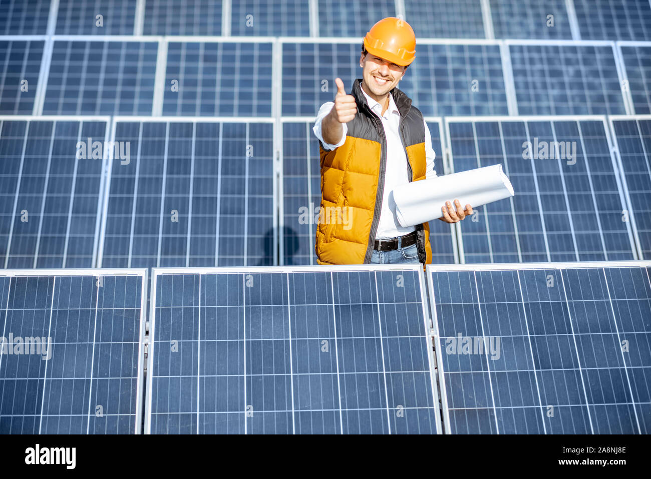 Ritratto di un ingegnere bello nel casco protettivo in piedi con blueprint su una centrale solare. Stazione solare concetto di sviluppo Foto Stock