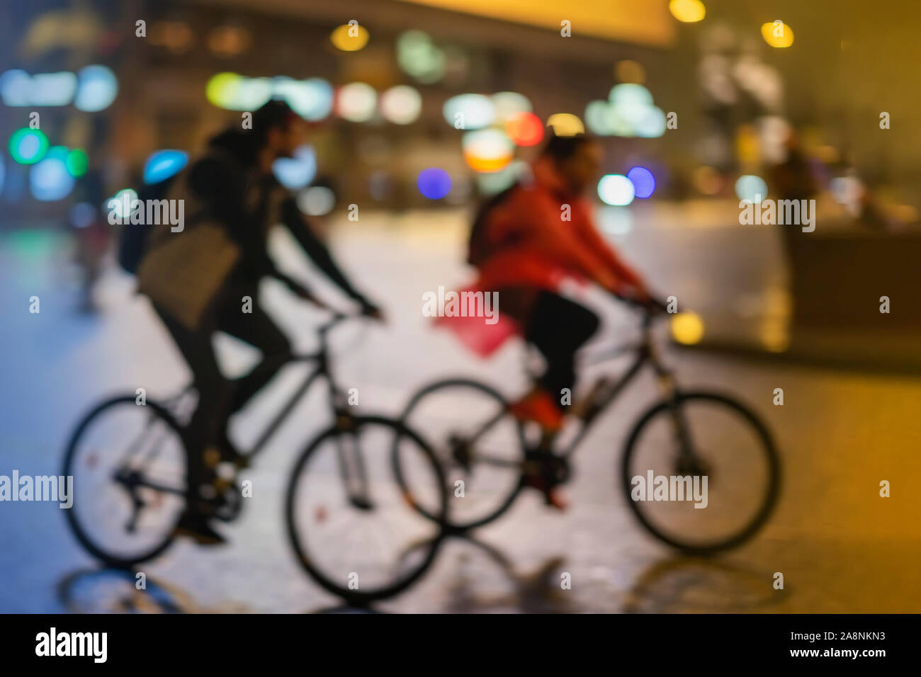 Sagome di astratta irriconoscibile coppia giovane, equitazione biciclette, night city, illuminazione bokeh, motion blur. Uno stile di vita sano, le attività per il tempo libero Foto Stock