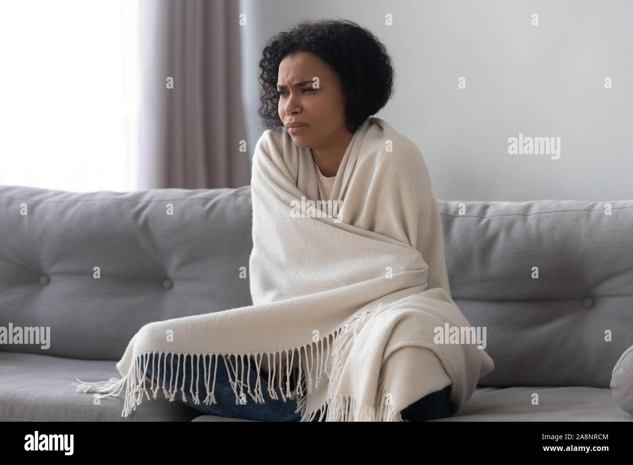 Infelice americano africano donna sensazione di freddo, coperto con la calda coperta Foto Stock