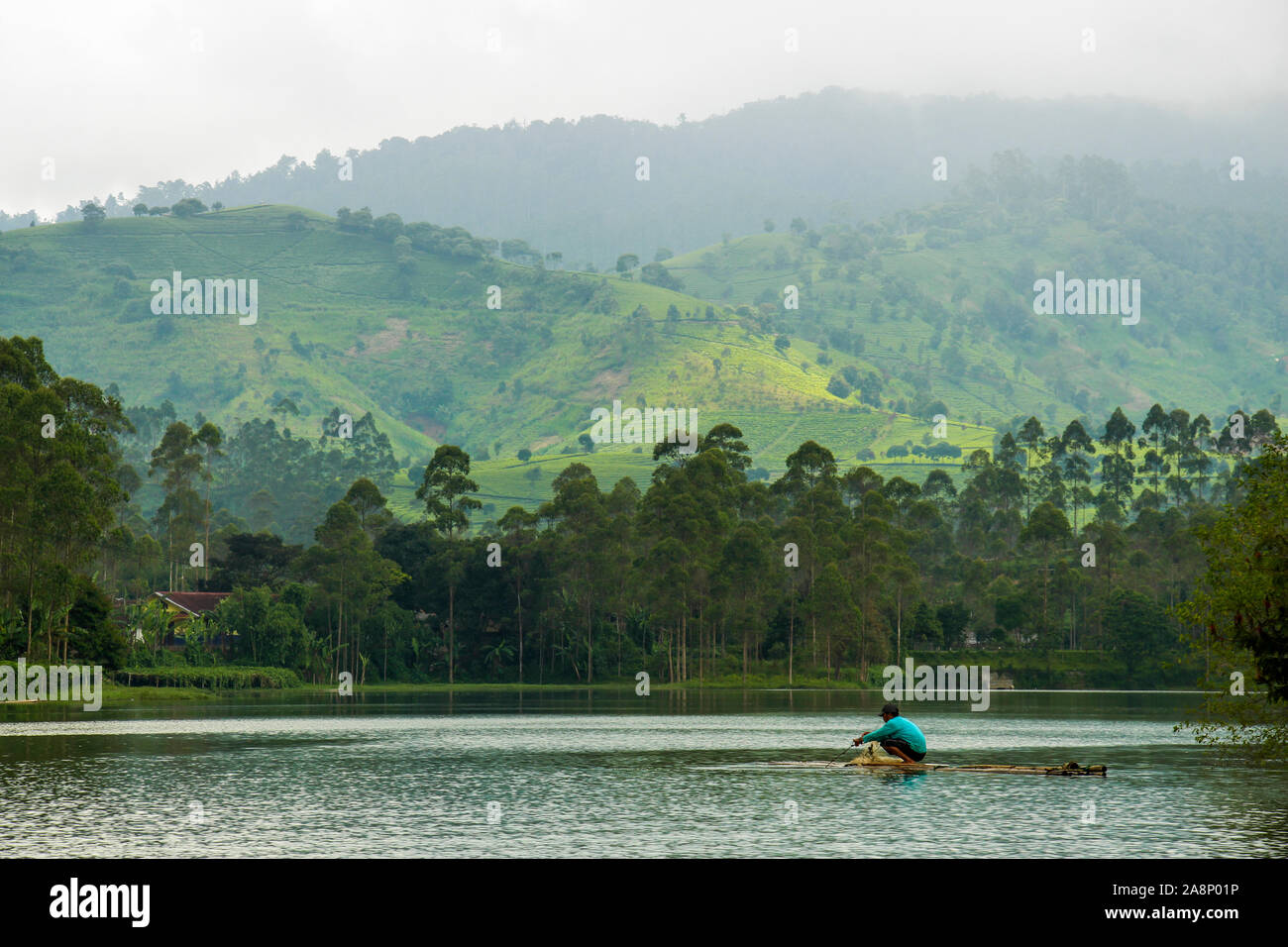 Pescatore indonesiano su zattera di bambù con collina in background, al Lago Cileunca, Pangalengan, Bandung, West Java, Indonesia Foto Stock