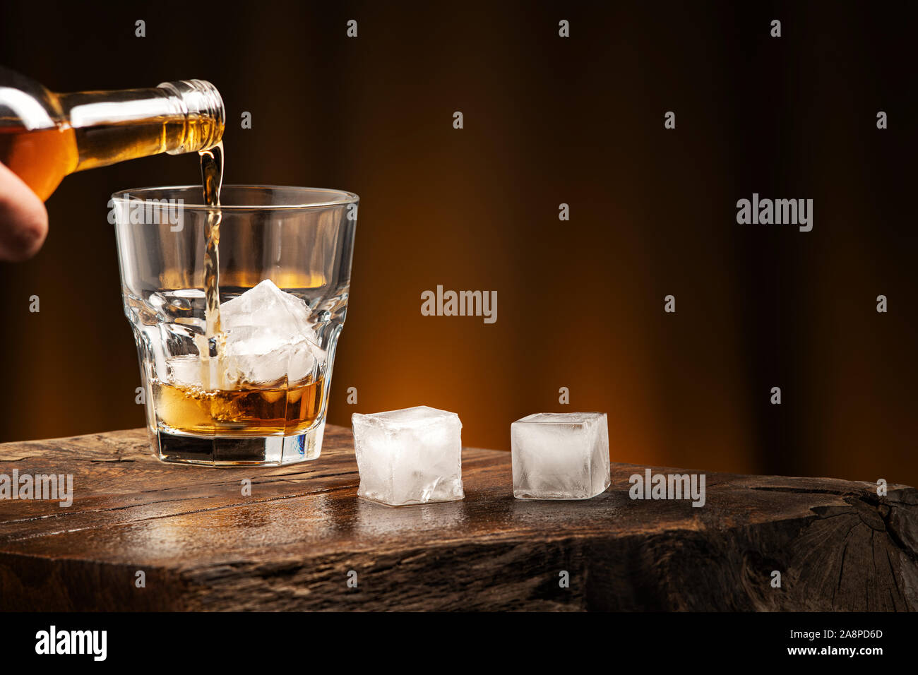 Colata di whiskey in un bicchiere con ghiaccio. Un bicchiere di bevanda alcolica su un tavolo di legno. Foto Stock
