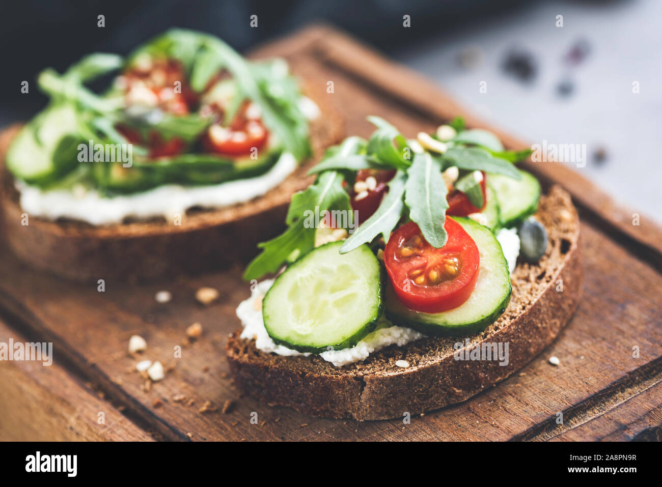 Pane di segale con crema di formaggio e cetriolo toast guarnito con pomodoro ciliegino, foglie di rucola e semi. Snack sani, puliti mangiare. Vista ingrandita, selezionare Foto Stock