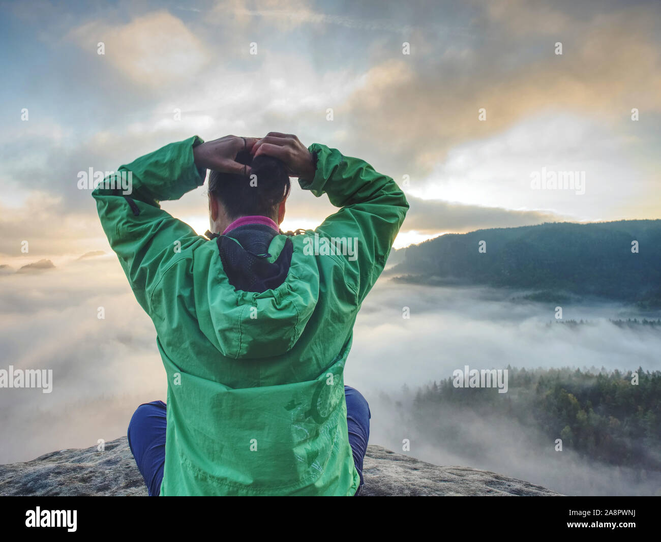 Donna sedersi sul bordo di scogliera e cercando di Rising Sun sopra la valle nebbiosa. Foggy mountain. L'uomo escursione Foto Stock