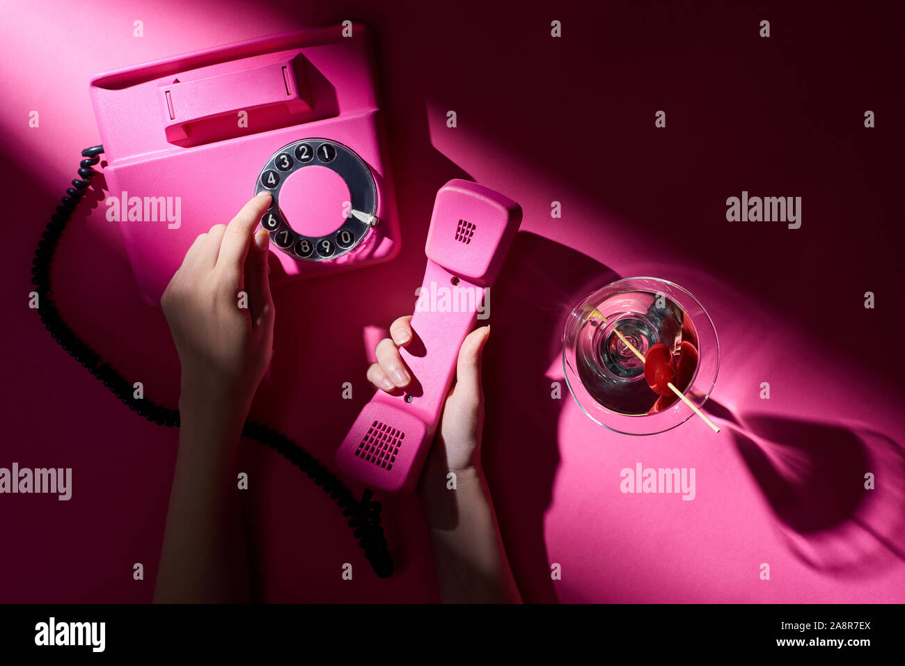 Vista ritagliata della donna tramite telefono retrò con martini accanto su sfondo rosa Foto Stock