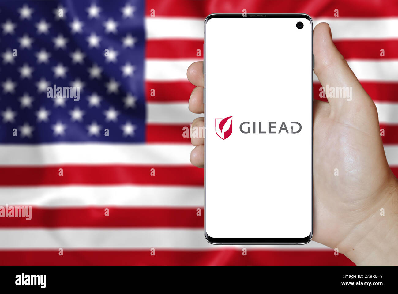 Il logo della società pubblica Gilead Sciences visualizzata su uno smartphone. Bandiera degli Stati Uniti sullo sfondo. Credito: PIXDUCE Foto Stock