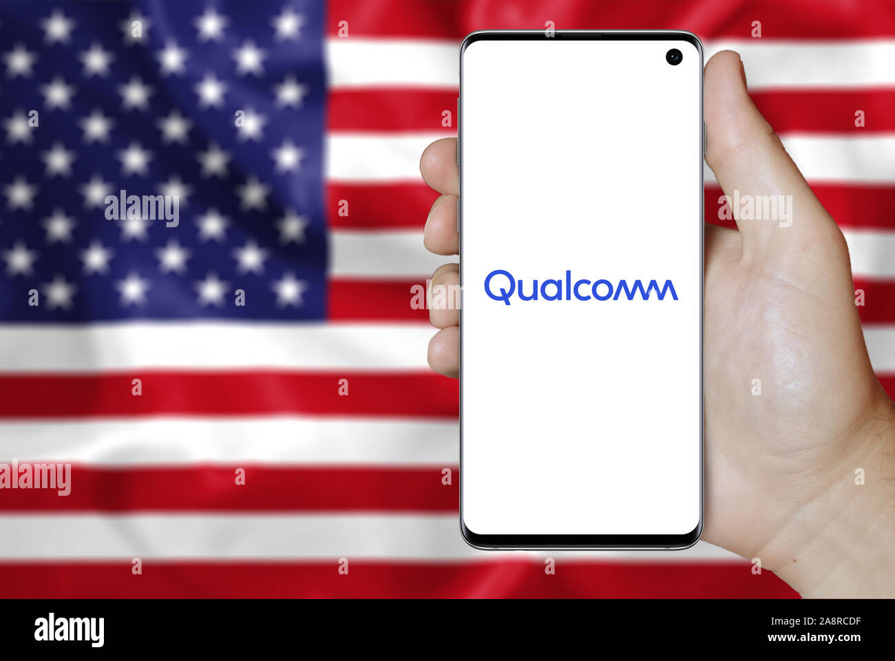 Il logo della società pubblica Qualcomm Inc. visualizzata su uno smartphone. Bandiera degli Stati Uniti sullo sfondo. Credito: PIXDUCE Foto Stock