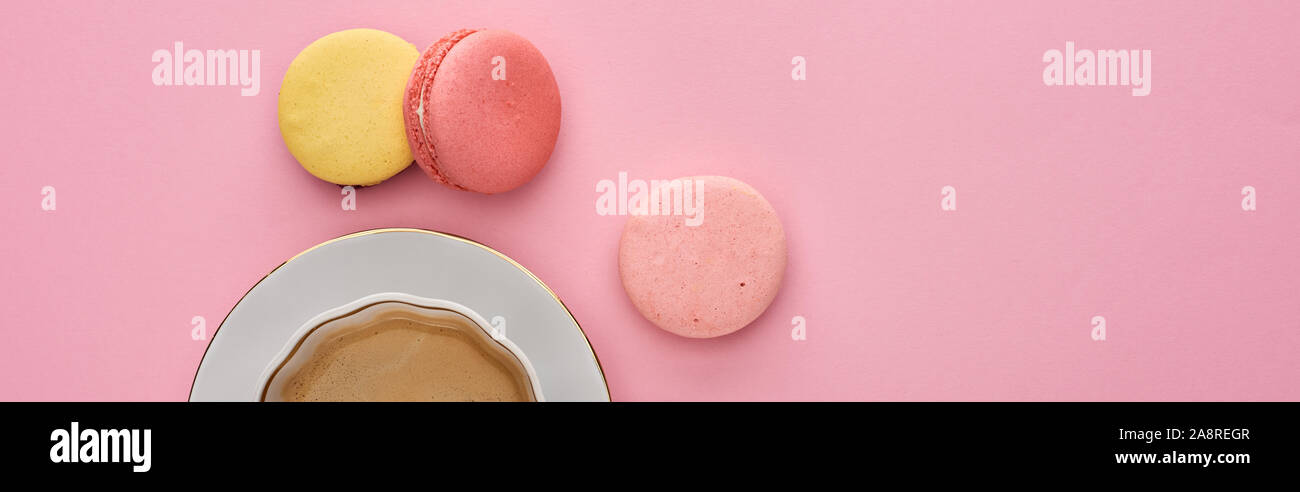 Vista dall'alto di deliziosi amaretti francese nei pressi di caffè in tazza sul piattino su sfondo rosa, scatto panoramico Foto Stock