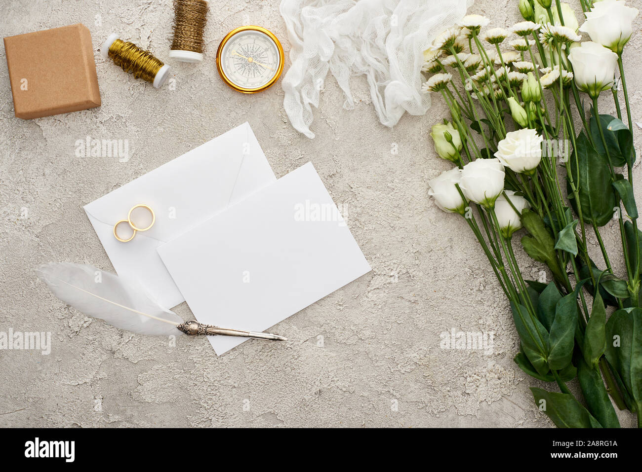 Vista superiore della scheda vuota vicino gli anelli di nozze, quill penna, bussola, garza e fiori sulla superficie testurizzata Foto Stock