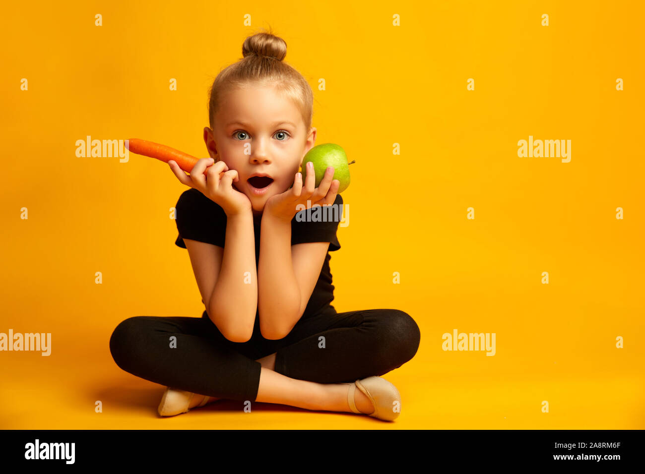 Perplesso little ballerina scegliendo tra una mela verde e una carota Foto Stock