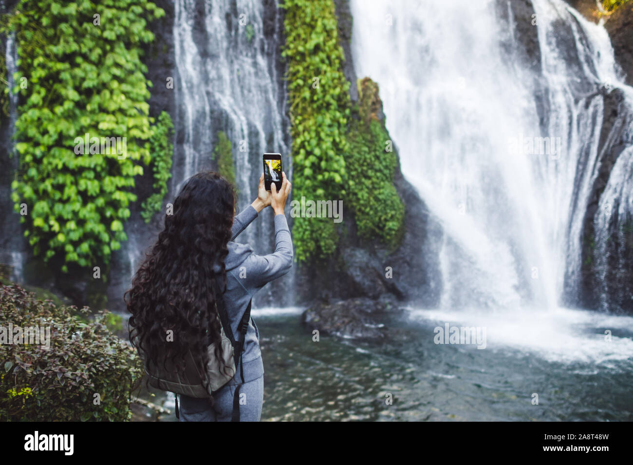La donna sta immagine di cascata Banyumala in Bali. Lunga parentesi brunette capelli, zaino. Concetto di viaggio. Foto Stock