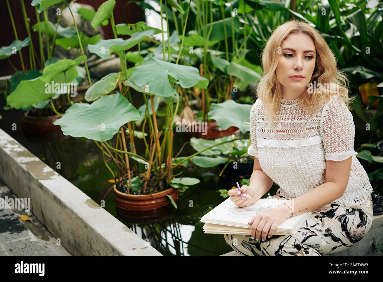 Bella grave giovane donna di trascorrere del tempo nel giardino di fiori e piante di disegno Foto Stock