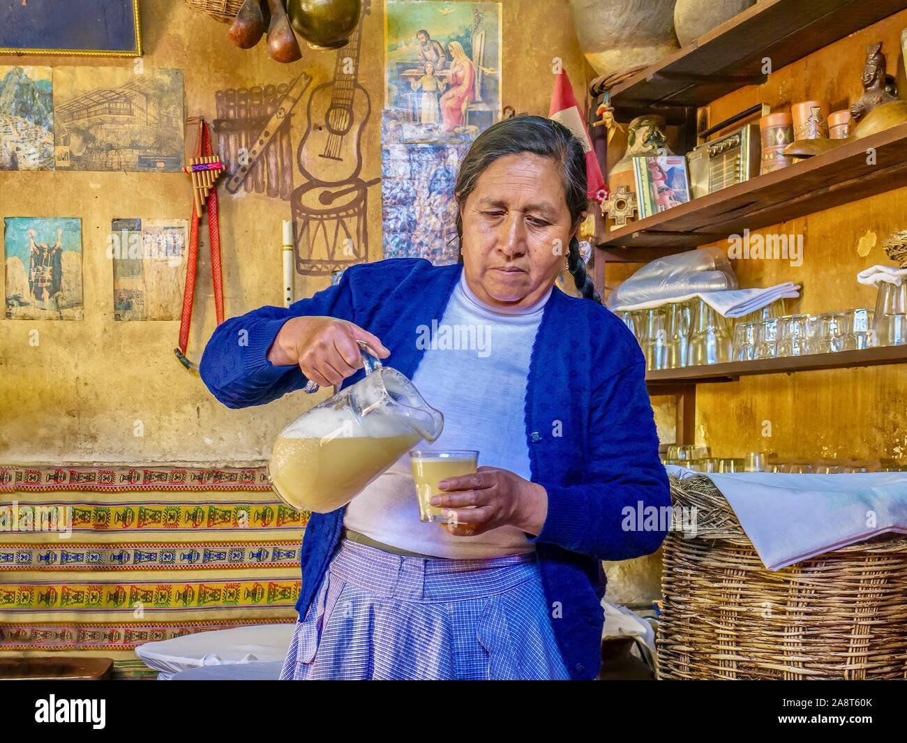 Una donna peruviana versando chicha, il tradizionale giallo fermentato drink andina realizzato da mais, da una brocca in una taverna noto come una chicheria. Foto Stock