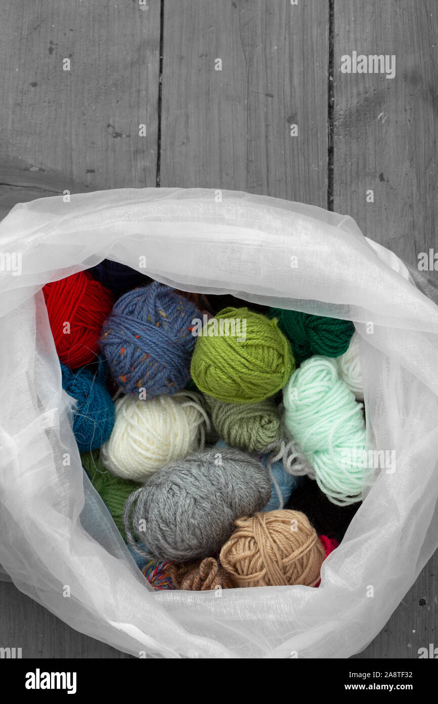 Palle di filati di lana in una selezione di colori e stili in una borsa bianca. Pavimento in legno sfondo con colore selettivo Foto Stock
