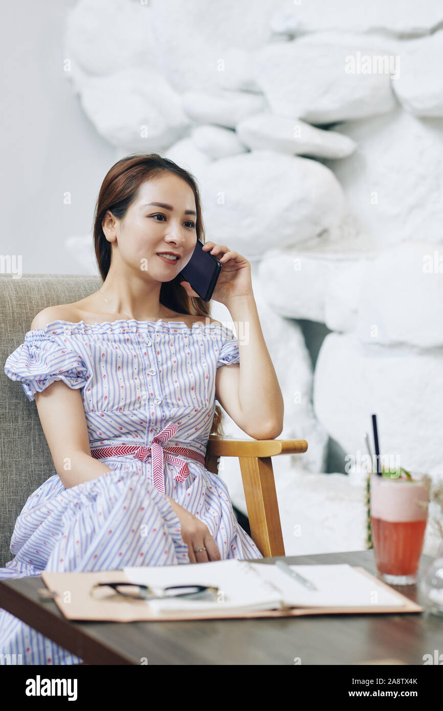 Bella giovane donna asiatica di bere cocktail di frutta in cafe e chiamando al telefono con un amico Foto Stock