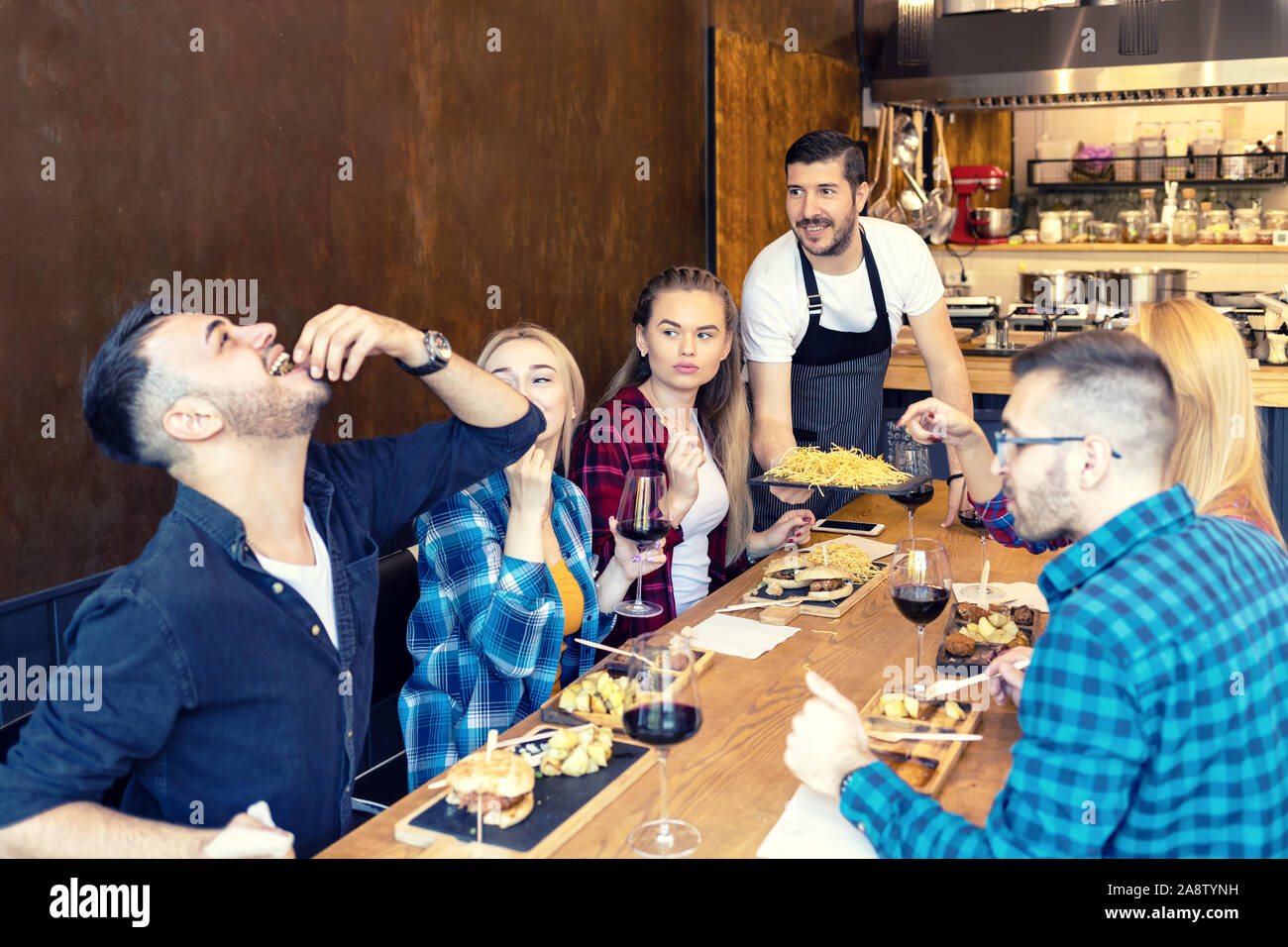 Gruppo dei migliori amici di mangiare il cibo gustoso nel piccolo ristorante mentre felice proprietario di servire loro Foto Stock