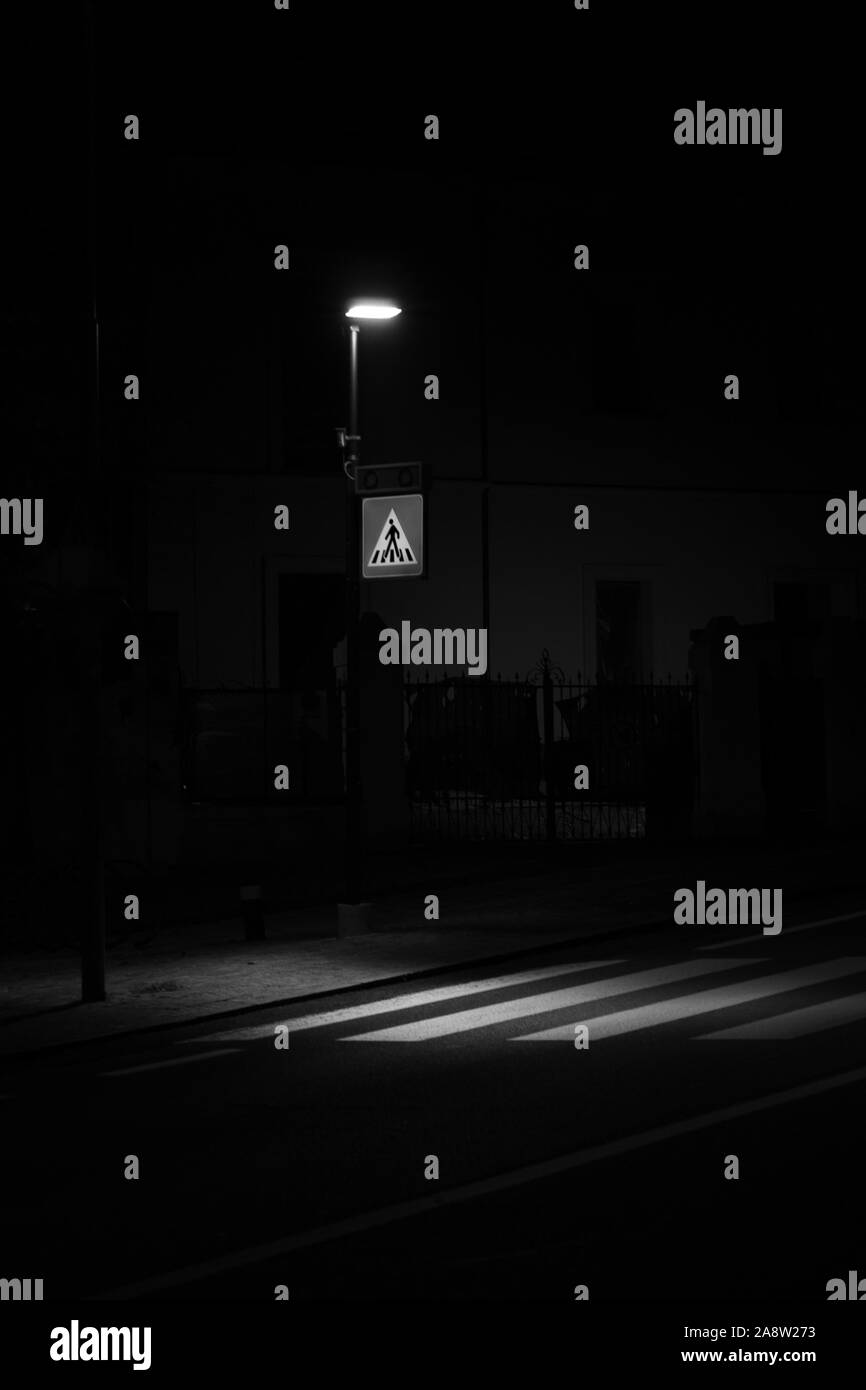 In bianco e nero girato di una strada lampada che illumina il passaggio pedonale di notte, impresso sulla carreggiata, per la sicurezza dei pedoni Foto Stock