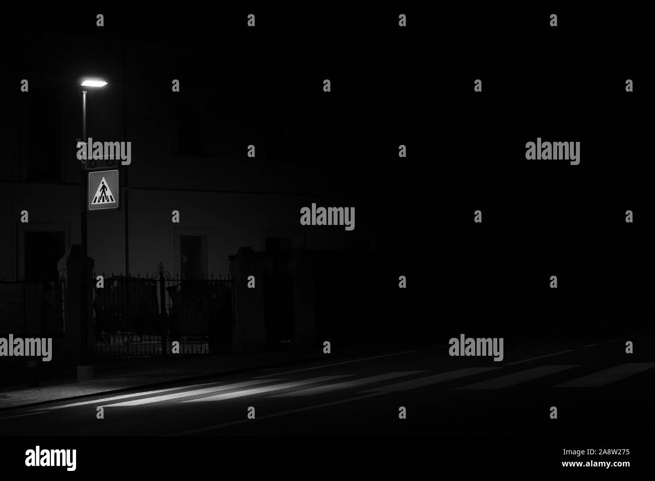 Girato in bianco e nero di una strada lampada che illumina il passaggio pedonale di notte, impresso sulla carreggiata, per la sicurezza dei pedoni Foto Stock