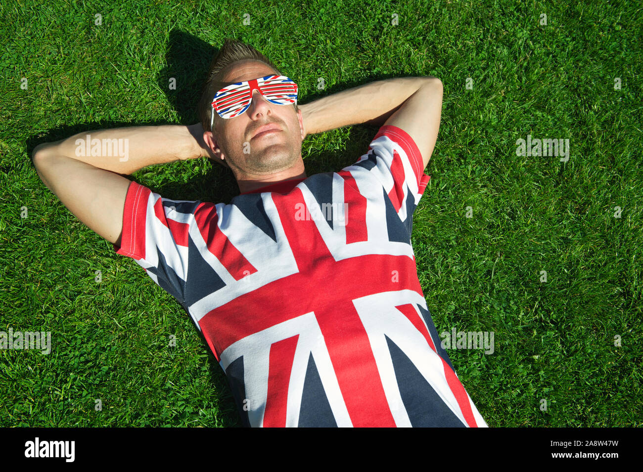Patriotic giovane in Unione Jack T-shirt occhiali da sole e relax su una patch di grande prato inglese Foto Stock