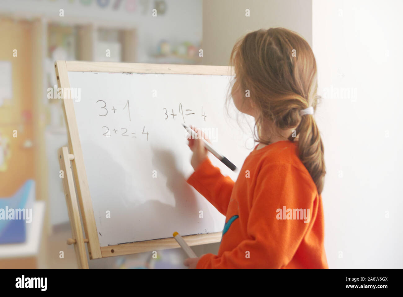 Bambino caucasico ragazza la risoluzione di addizione matematica operazione su una lavagna bianca in un'aula. Svuotare lo spazio di copia per l'editor di testo. Foto Stock