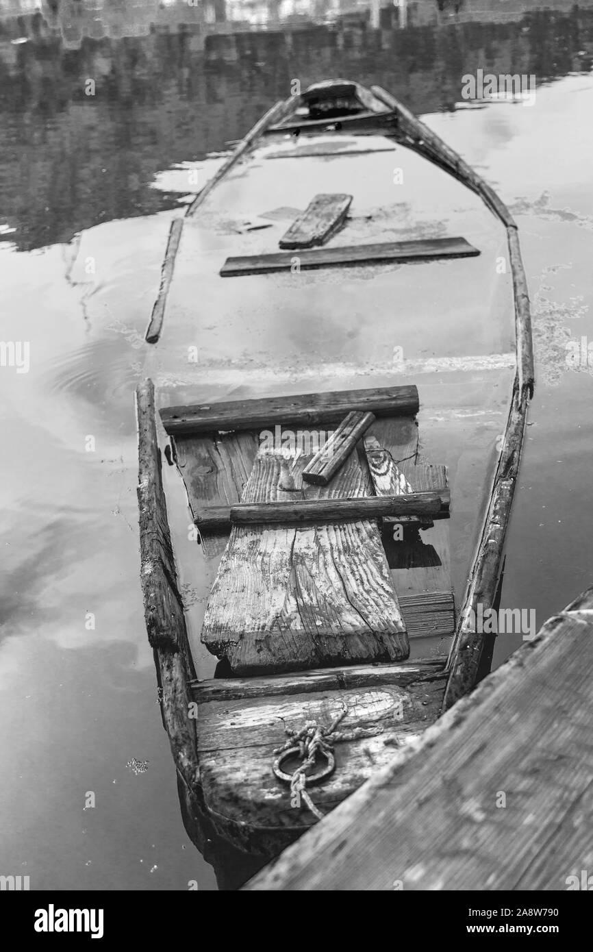 Vecchia barca in legno, canoa in un lago. Un rosso arancio imbarcazione in legno si trova sulle sponde di un lago, il riempimento con acqua Foto Stock